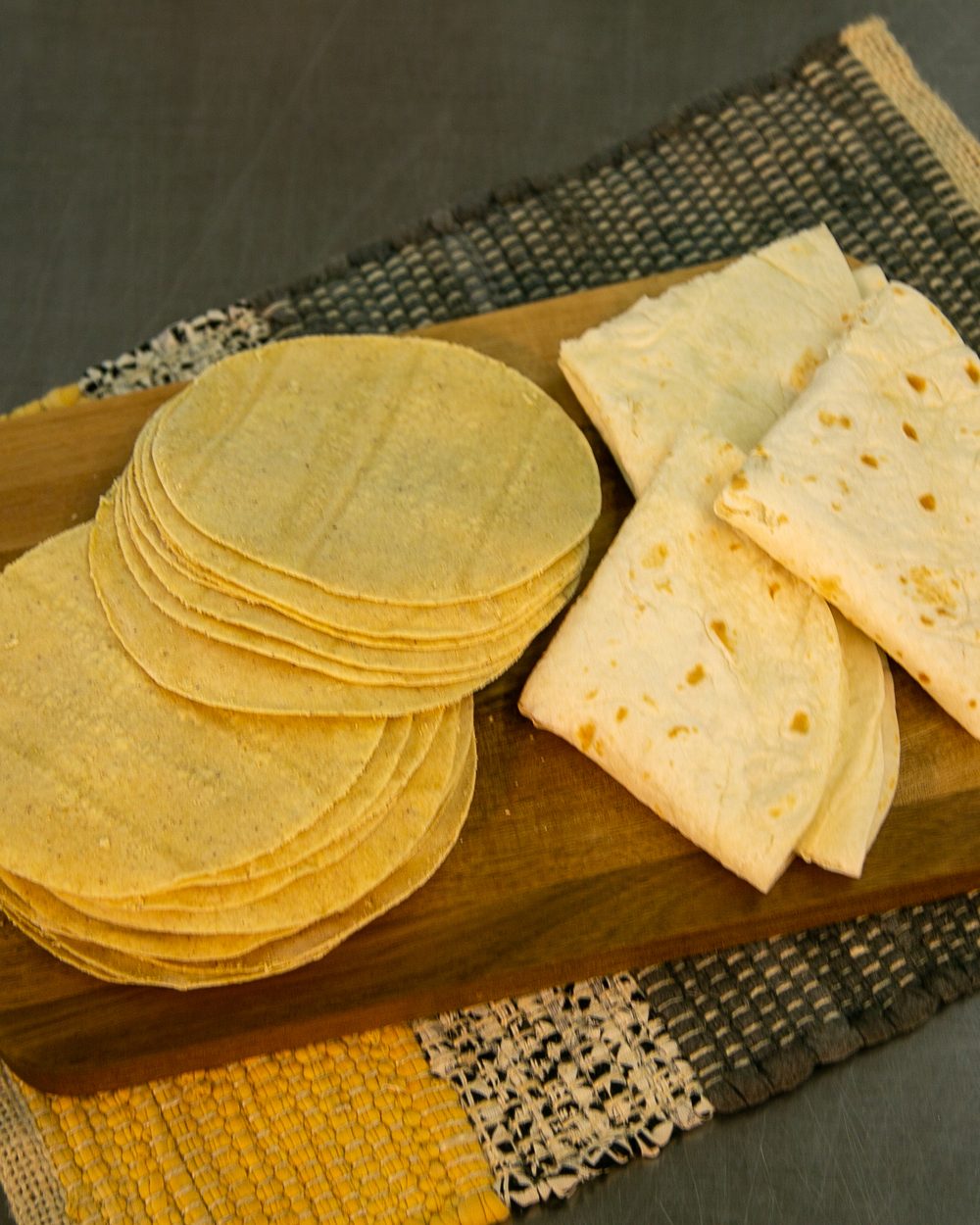 Close-up of a stack of Leal's flour tortillas showing texture and soft layers, warm amber light on dark background.