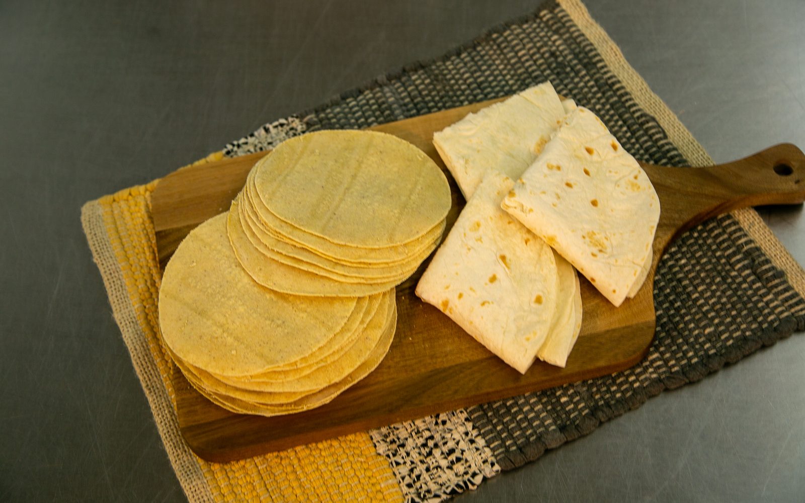 Tortillas de maíz frescas apiladas sobre una superficie de madera desgastada, luz ambar cálida, Fábrica de Tortillas Leal.